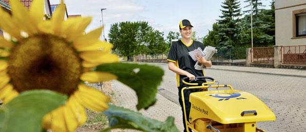 Zustellerin der Post mit Schiebewagen vor Sonnenblume